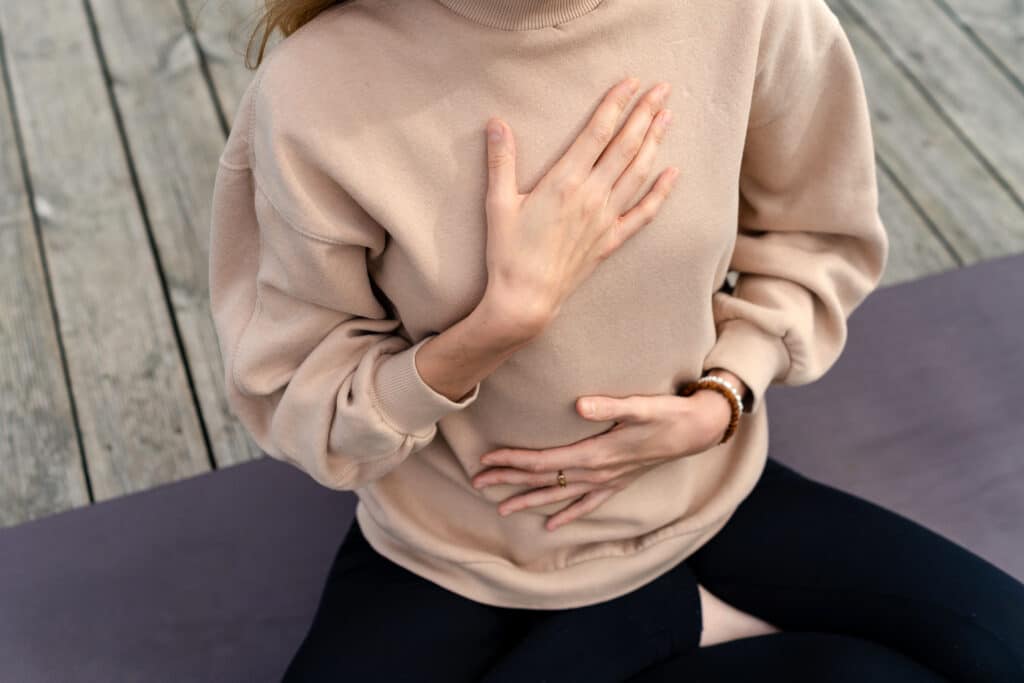 Femme en pull, mains sur poitrine et ventre pour méditation ou respiration consciente sur tapis de yoga. Calme, sérénité.